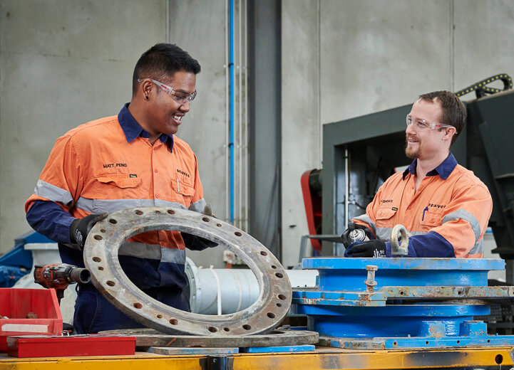 Two team members repairing and refurbing a large stainless steel knife gate valve